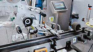 Labeling machine for sticking self-adhesive labels on top of caps and boxes